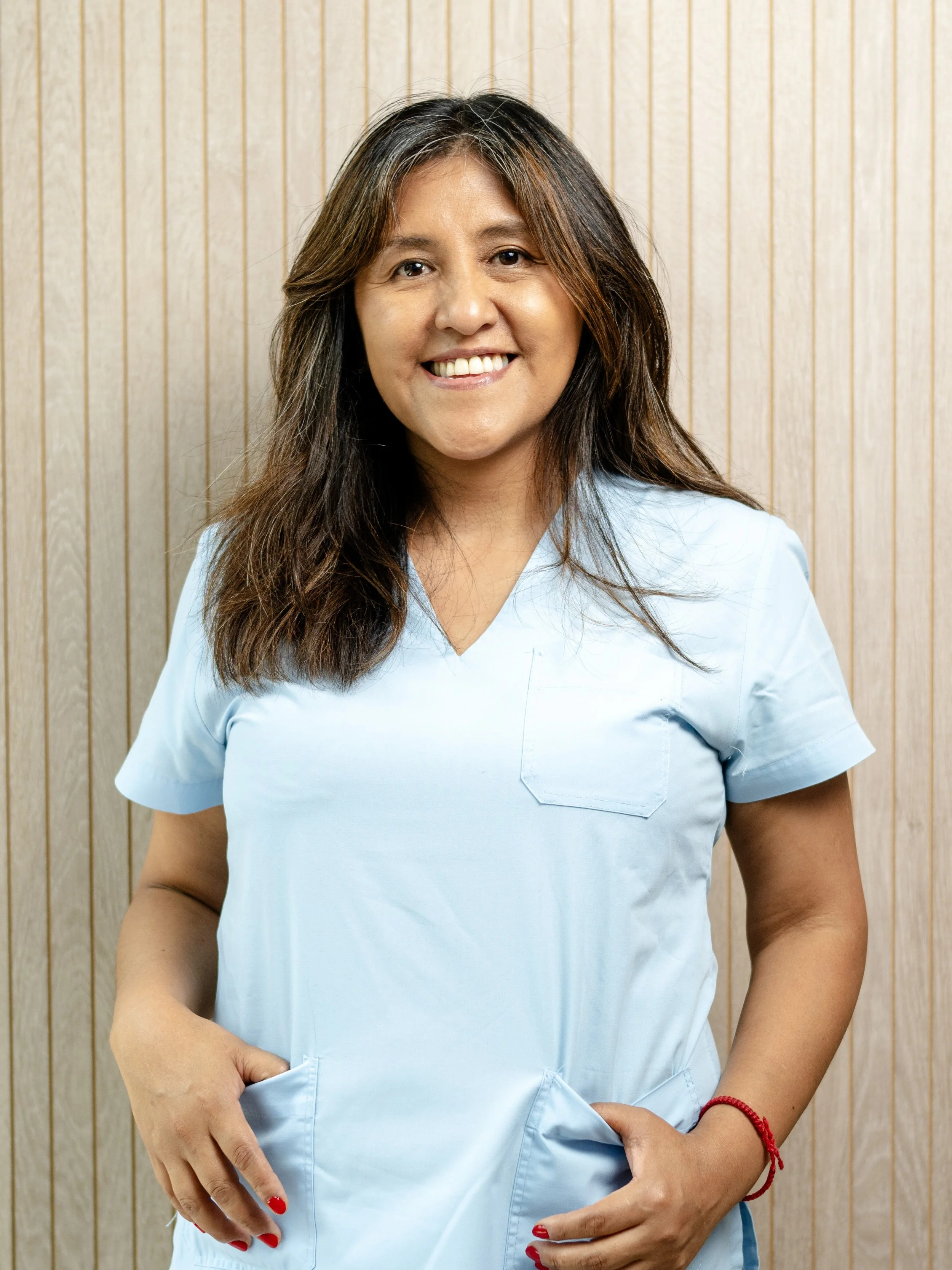 Mujer sonriendo con uniforme azul frente a fondo de madera