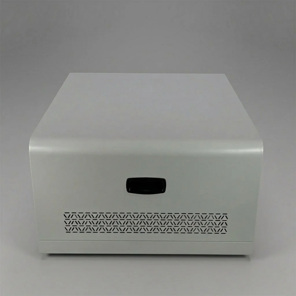 A white, modern electronic device with a black rectangular button and ventilation holes, placed on a white surface against a gray background.
