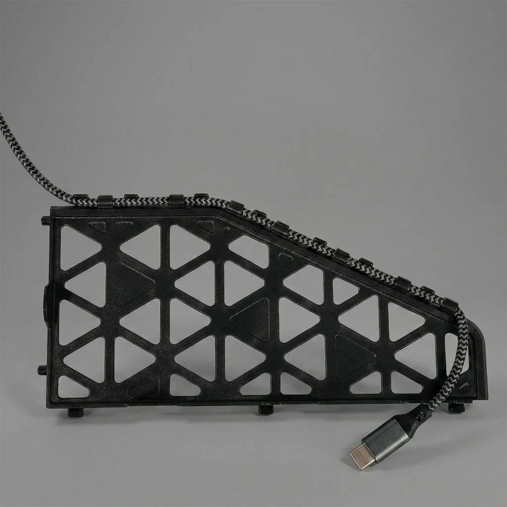 A black, triangular-shaped electronic device with a cable attached, placed on a gray background.