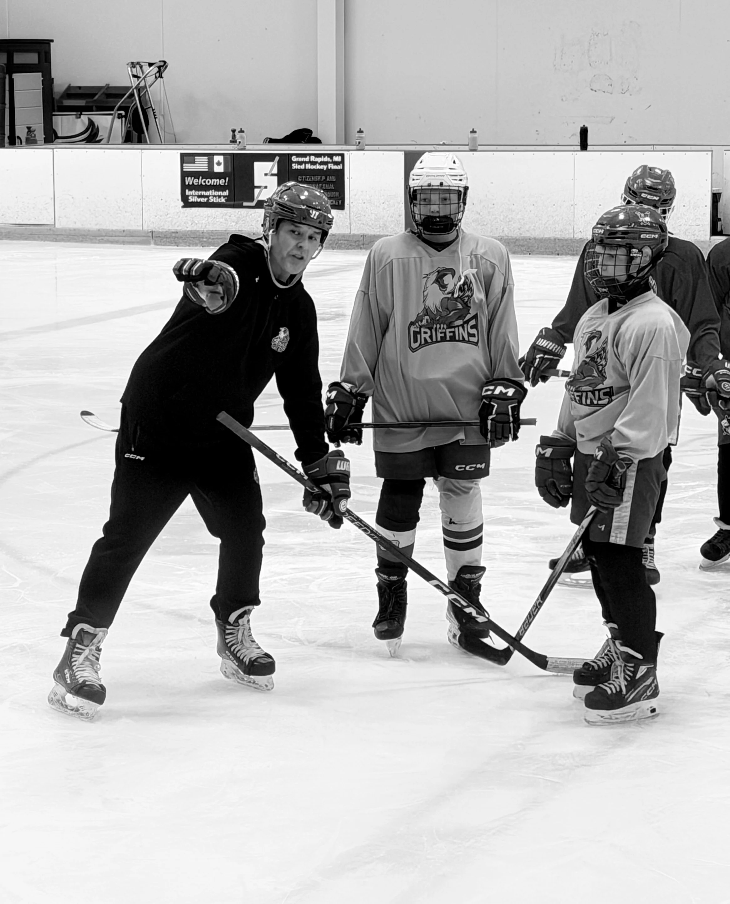 Hockey coach instructing young players during practice on an ice rink, all in hockey gear.