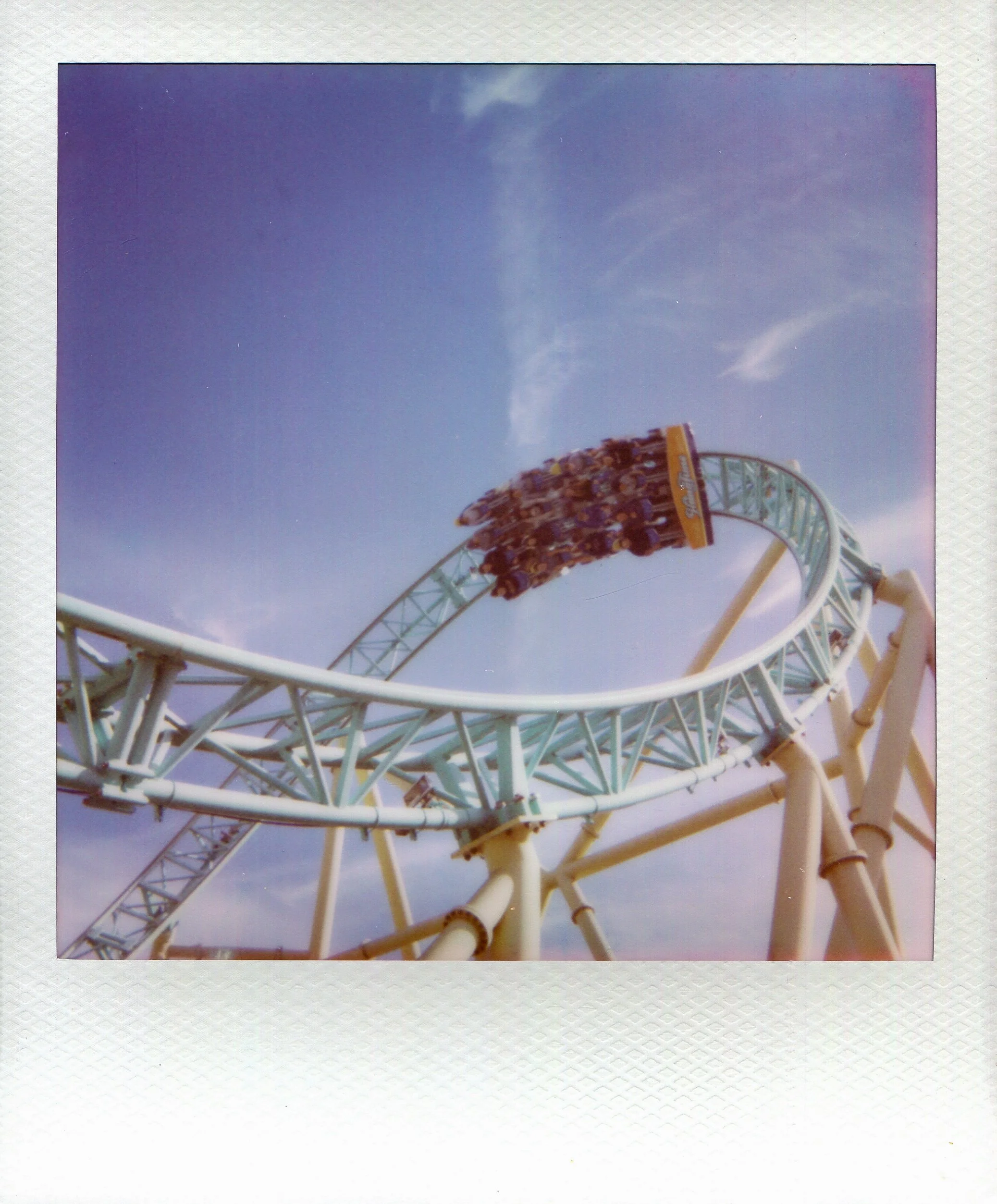 People riding a roller coaster with a loop at an amusement park against a blue sky.