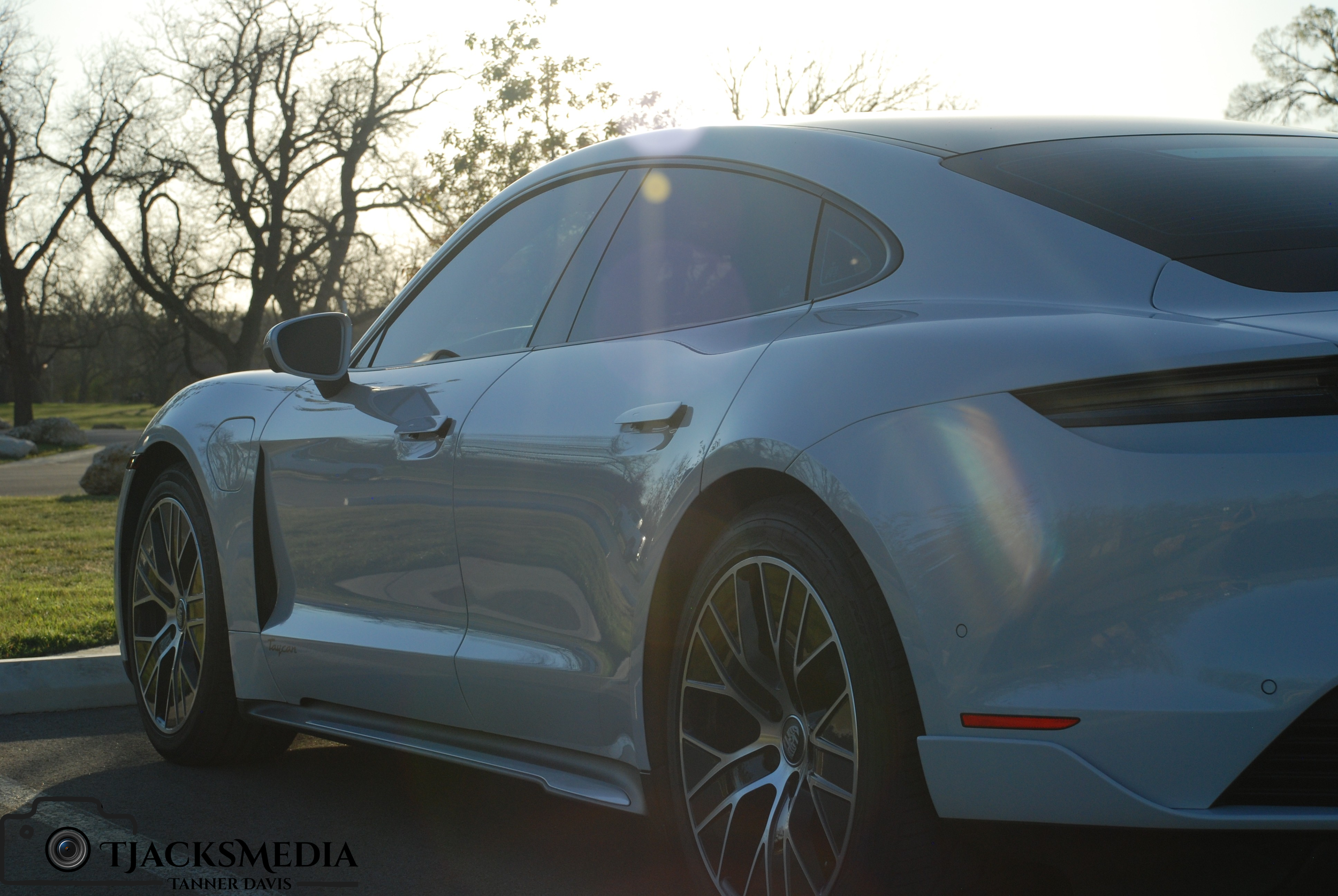 A sleek, sports car parked outdoors with trees in the background, sun flare, and bright sunlight.