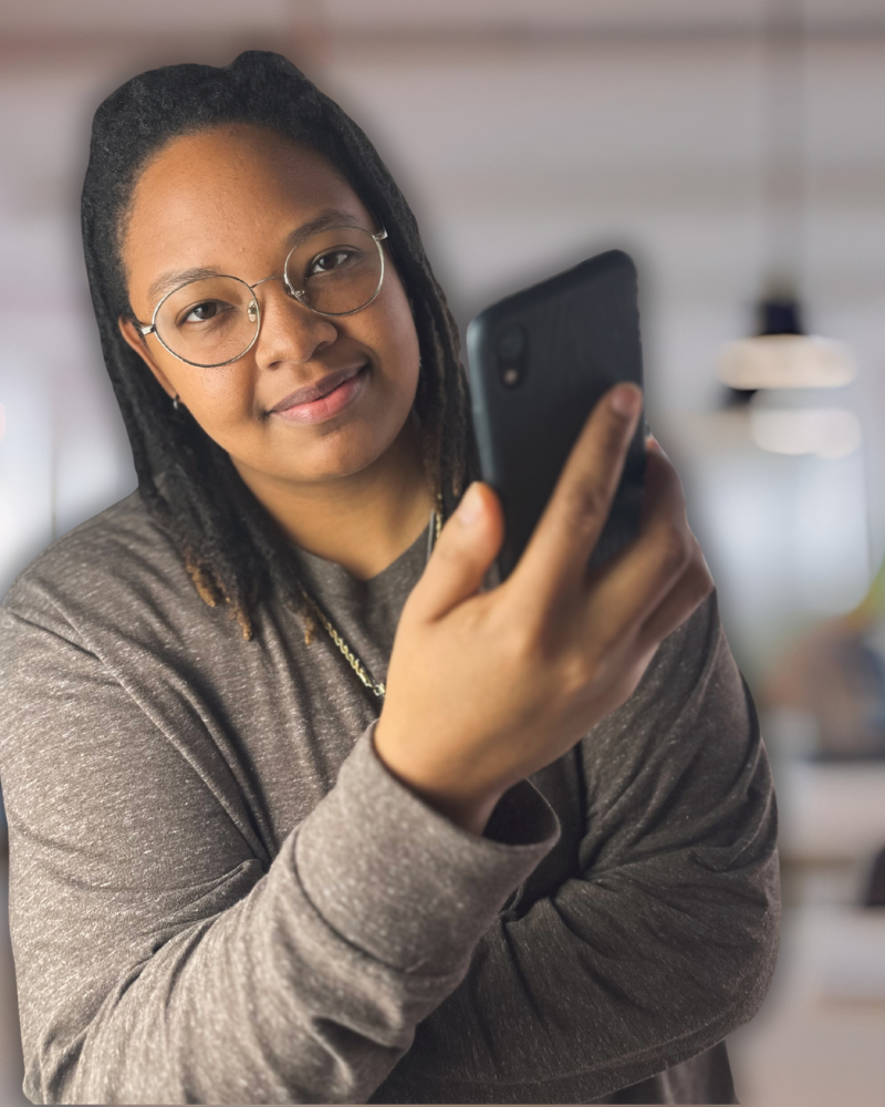 Young woman with glasses and dreadlocks taking a selfie with her smartphone in an indoor setting.