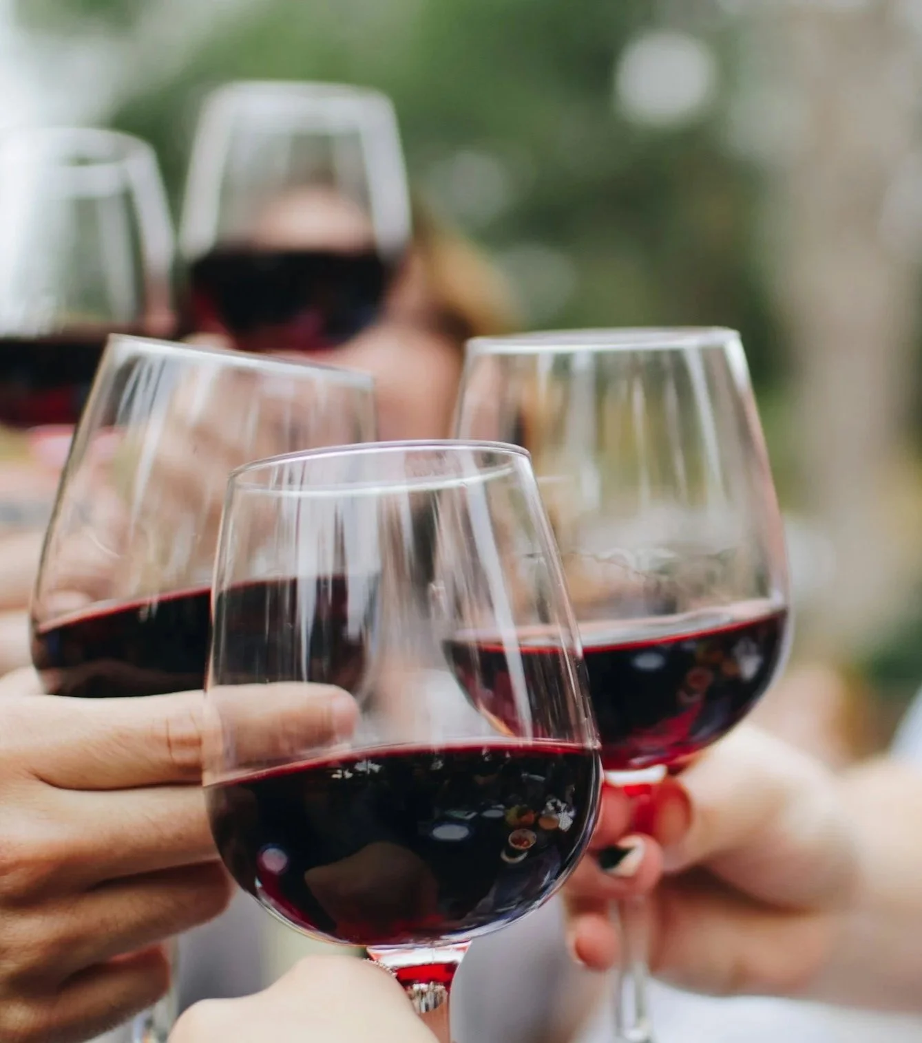 Four people clinking glasses of red wine at an outdoor gathering.