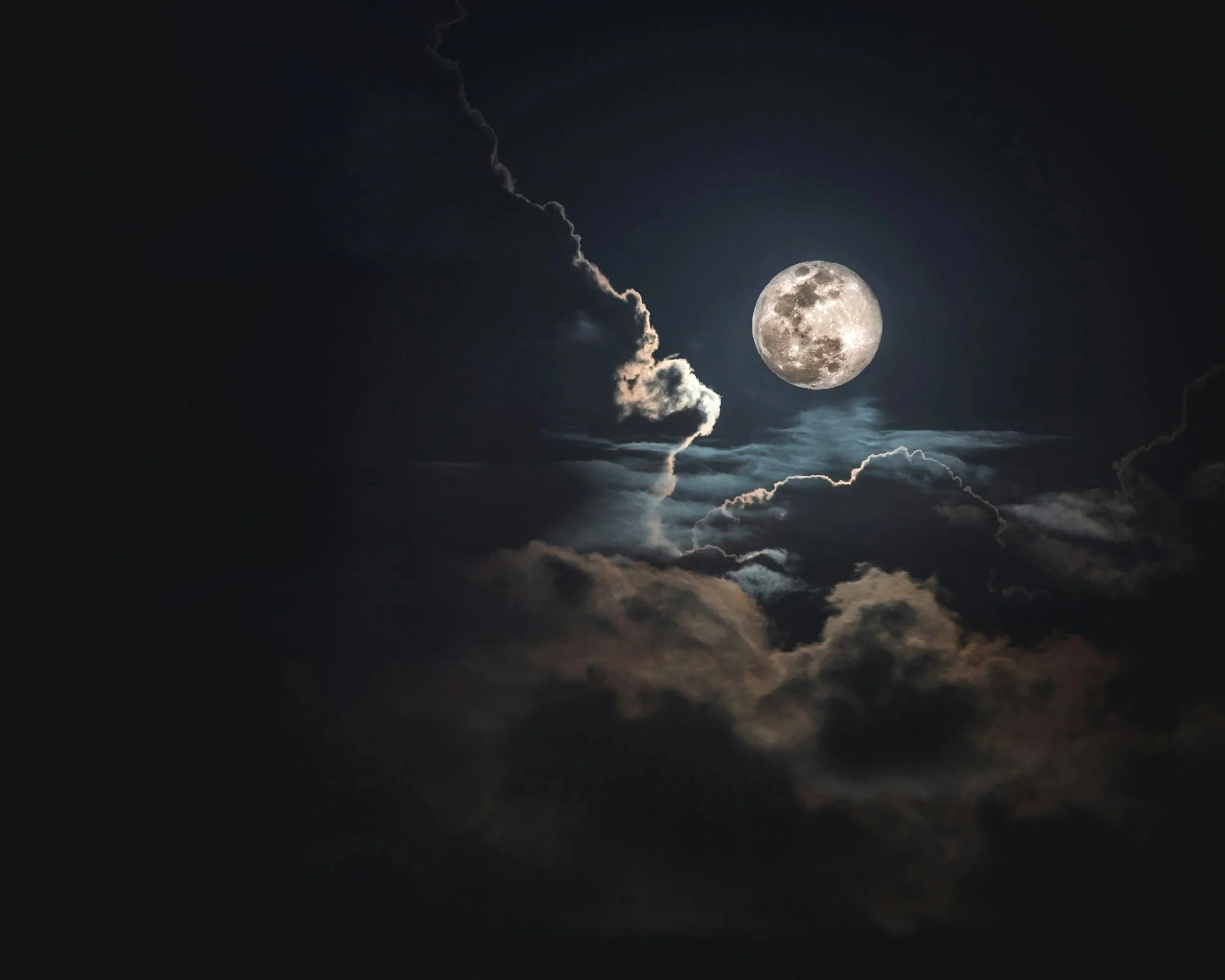 Full moon in a night sky with dark clouds.
