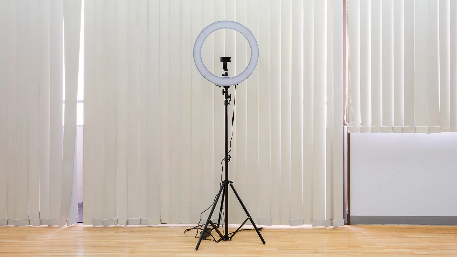 A ring light on a stand in front of vertical window blinds.