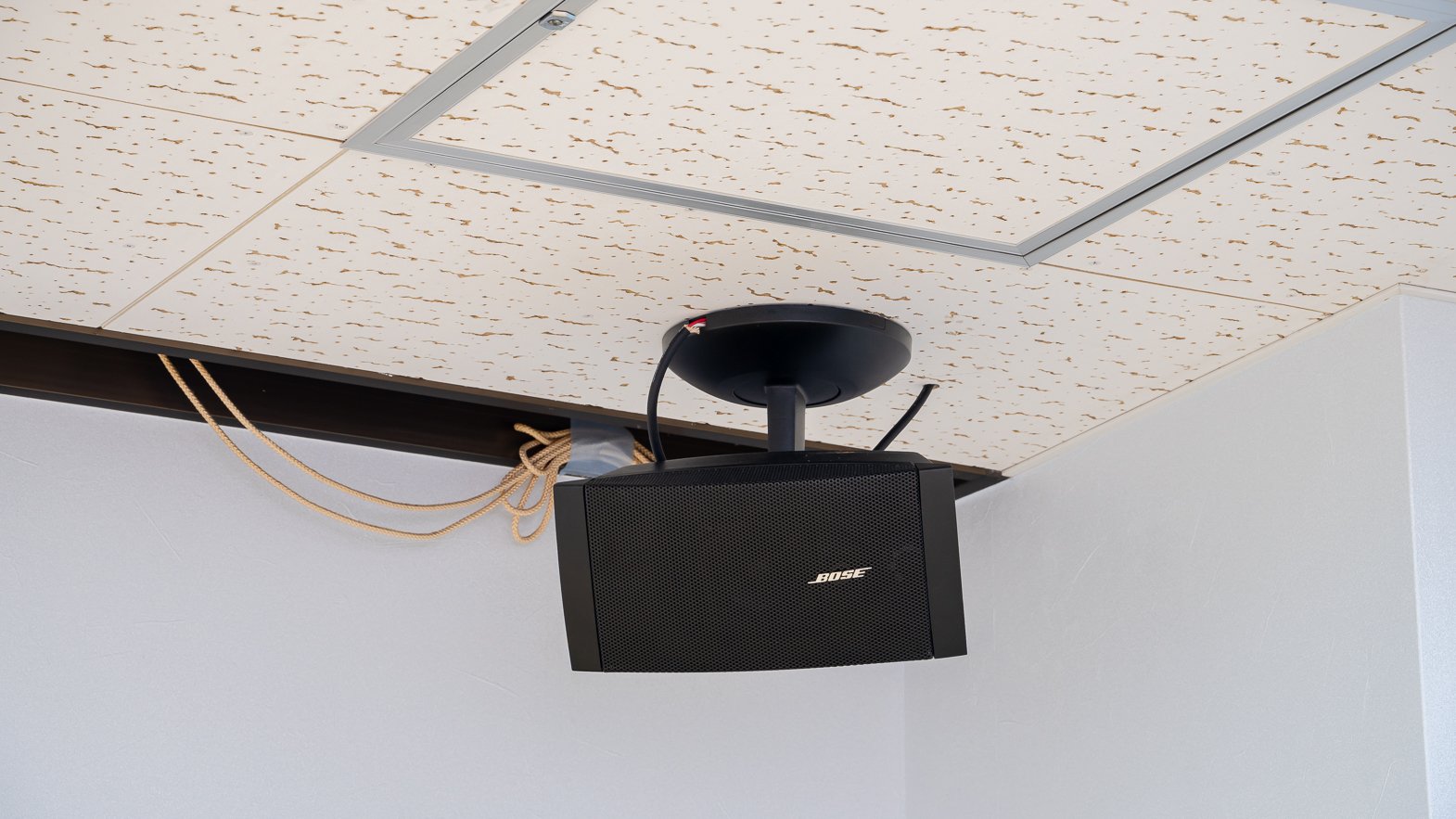 Black Bose speaker mounted under a patterned ceiling tile.