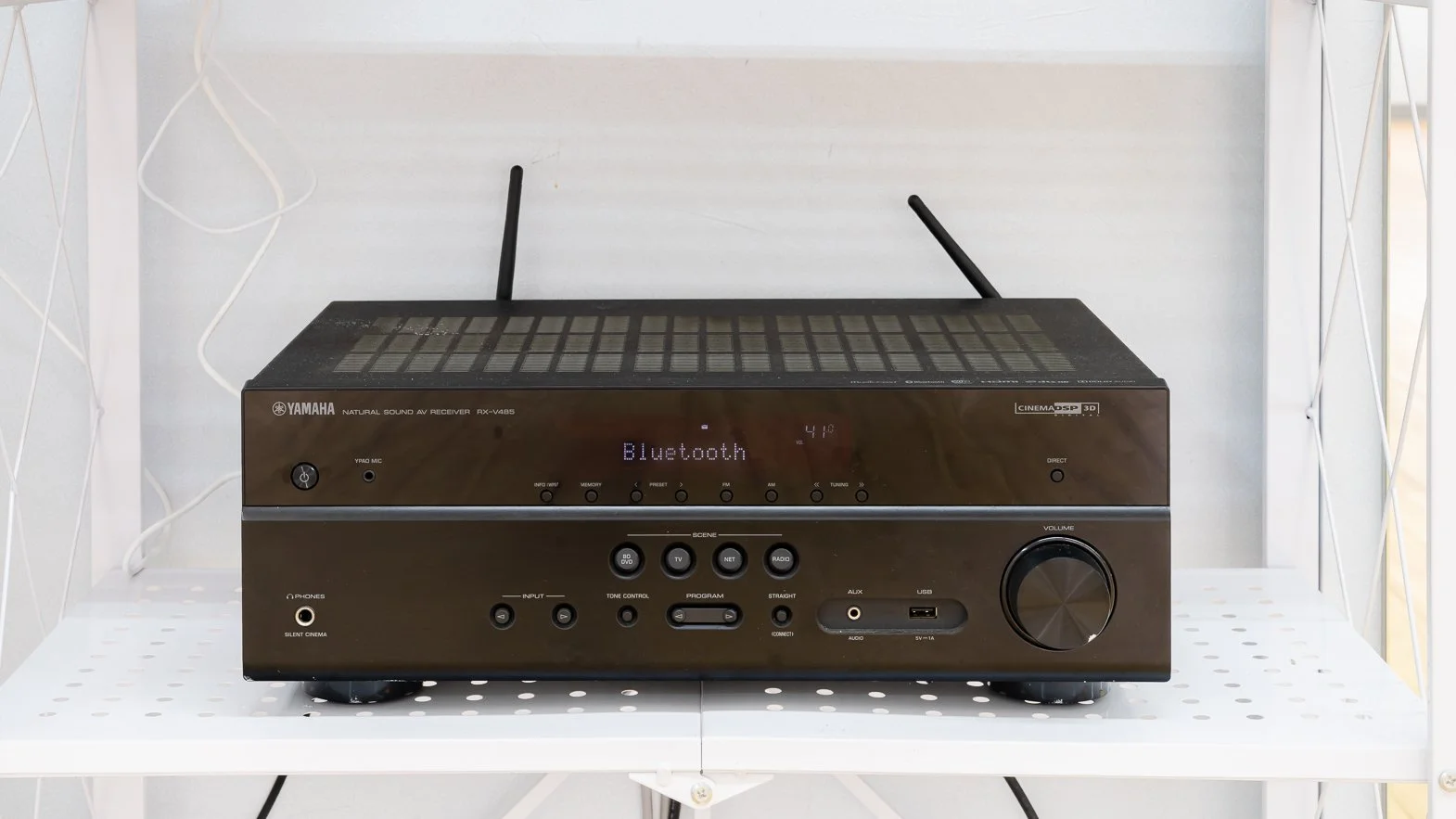 Yamaha audio receiver with antennas on top, placed on a white perforated table, displaying Bluetooth mode on its screen.