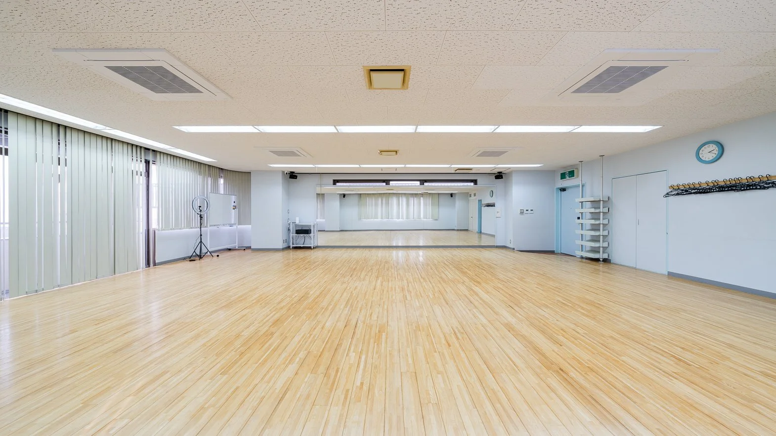Empty dance studio with hardwood floors, large mirror, and ceiling lights.