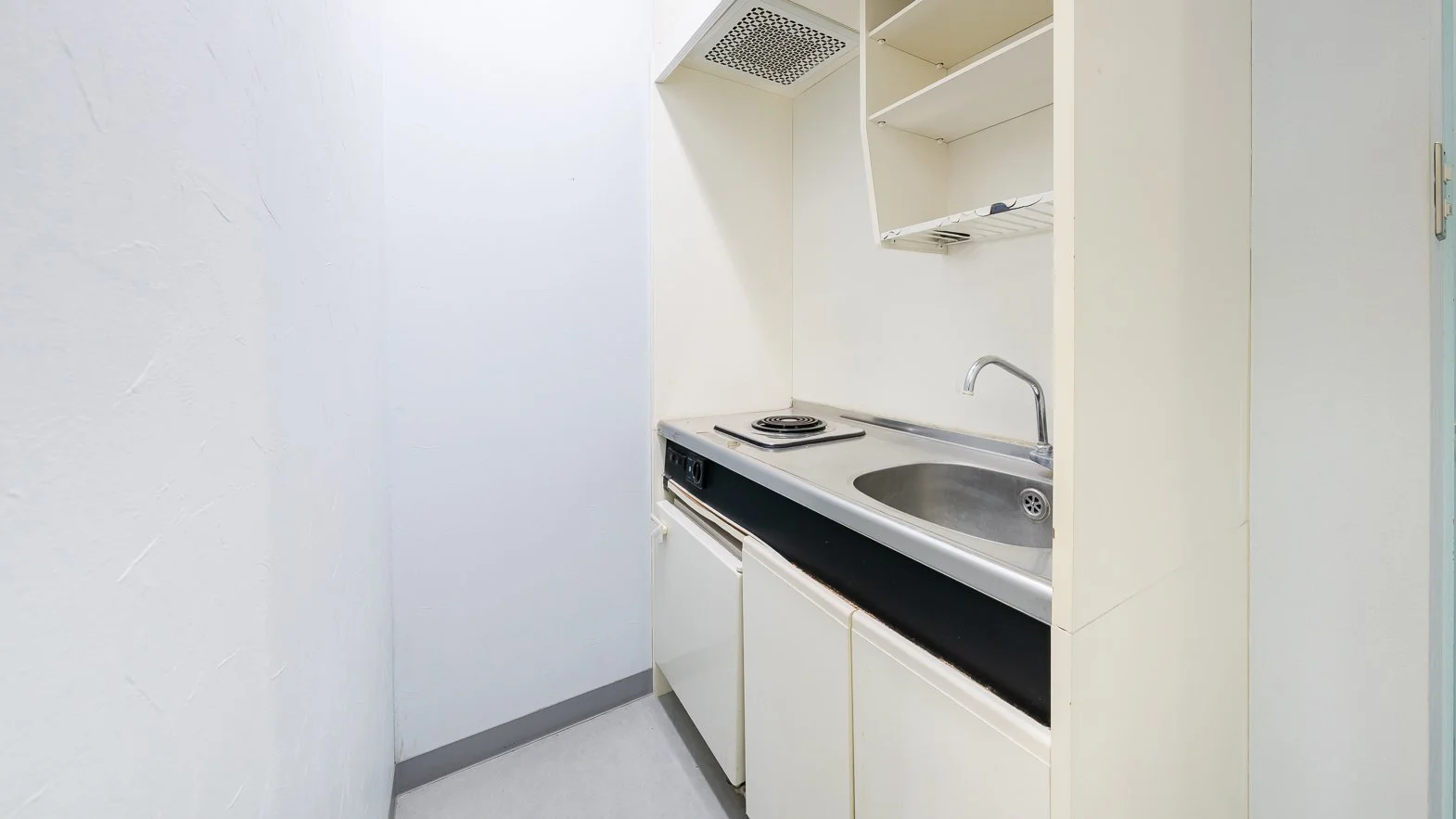 Small kitchenette with a sink, single electric burner stove, white cabinets, and open shelving.