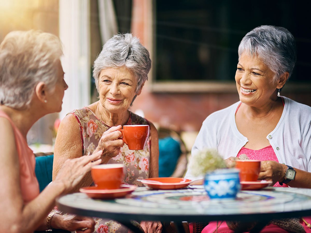 Three women sitting at a cafe table drinking coffee and talking together at the Tide & Times dementia cafe.