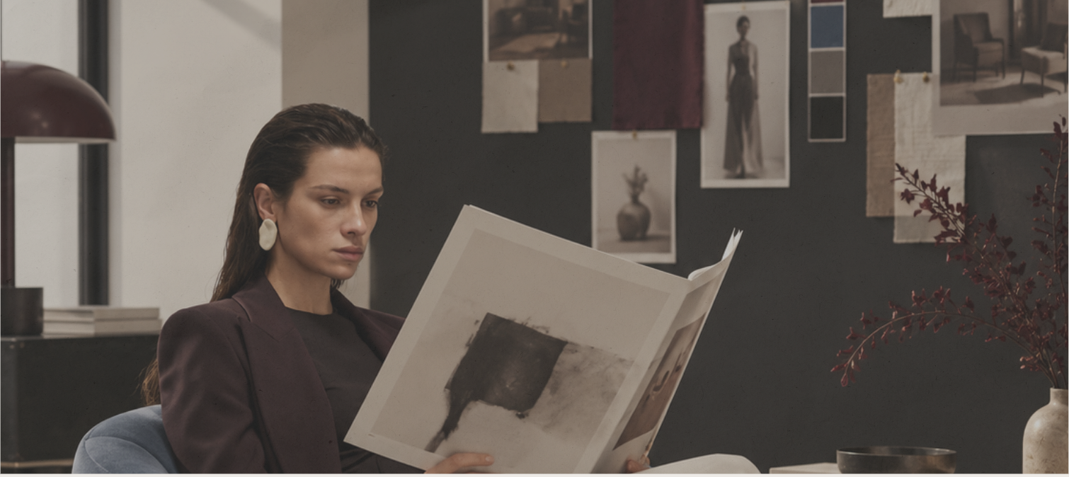 A woman reads a large-format magazine in front of a mood board.