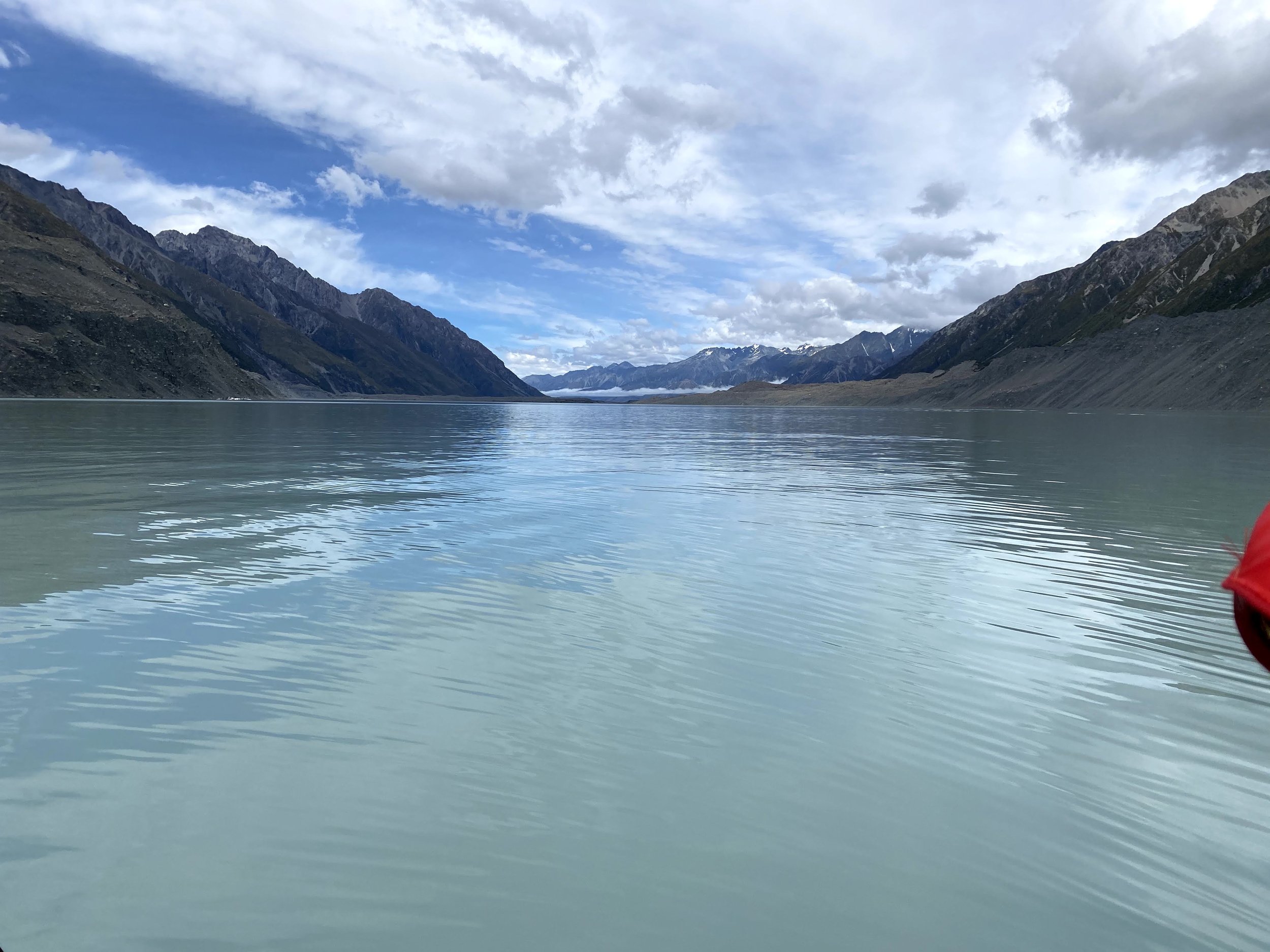 A calm, expansive lake surrounded by mountains under a partly cloudy sky.