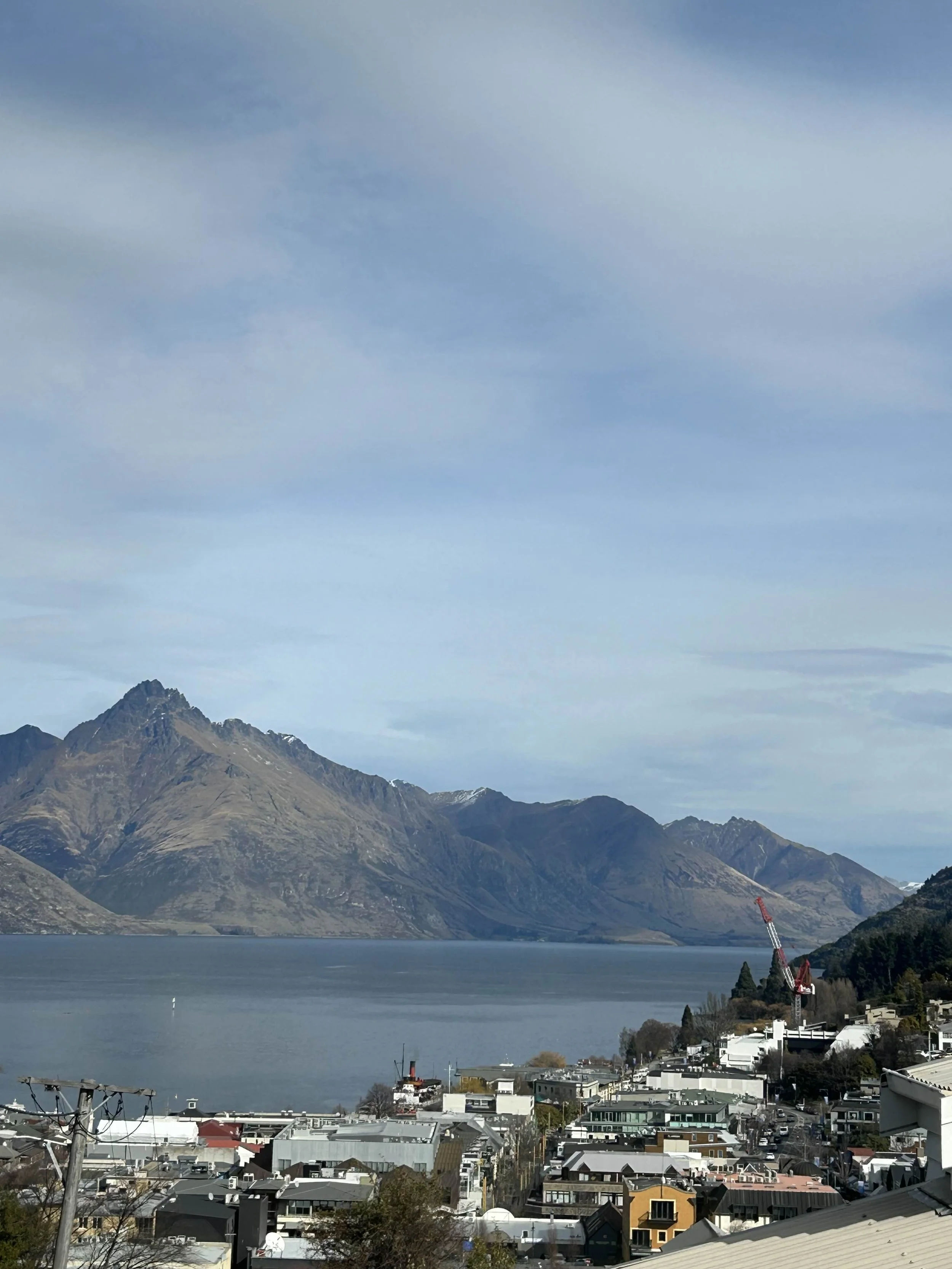 Cityscape with houses and a water body, mountains in the background, partly cloudy sky.