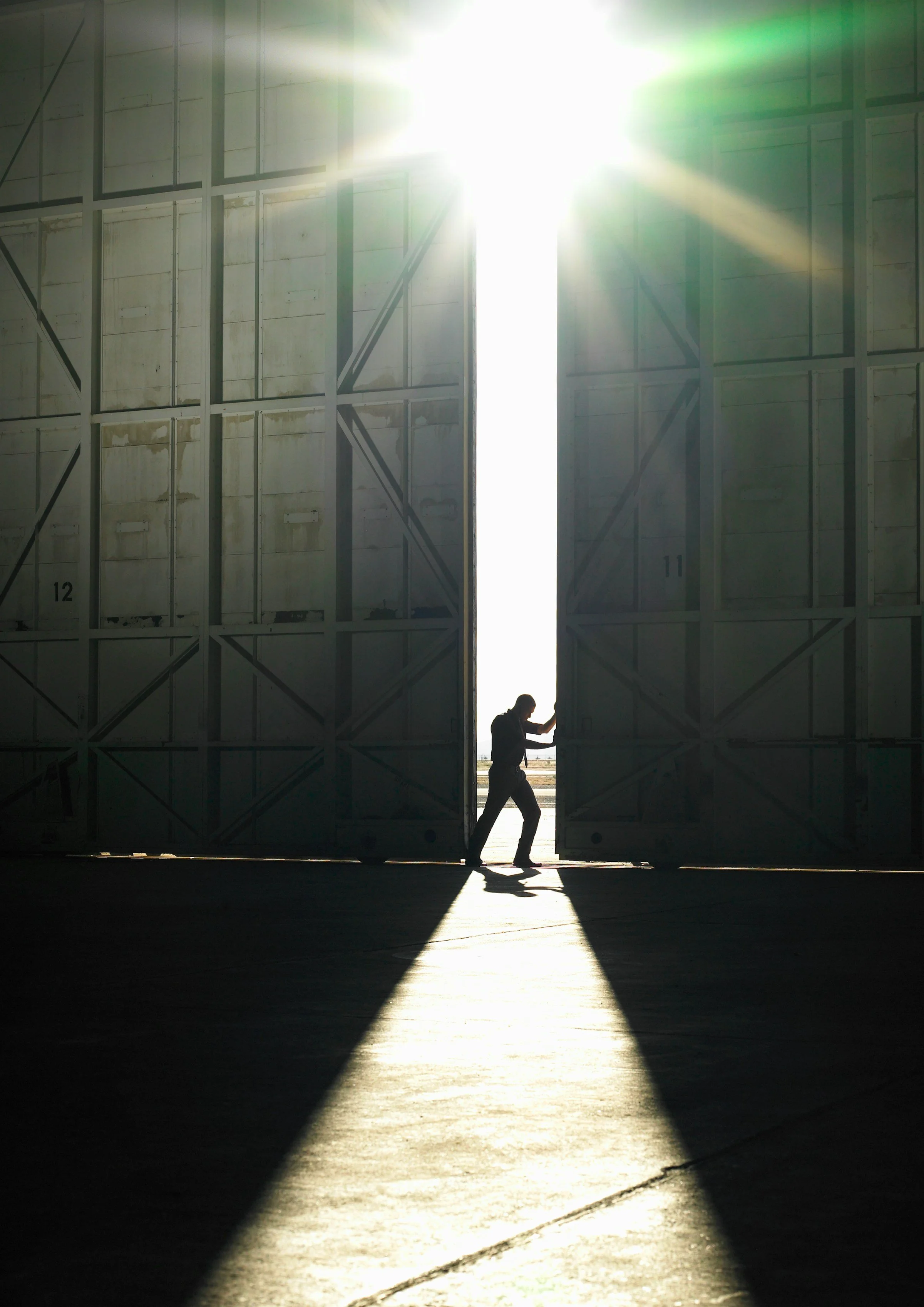 A person walking through large open hangar doors with sunlight streaming in.
