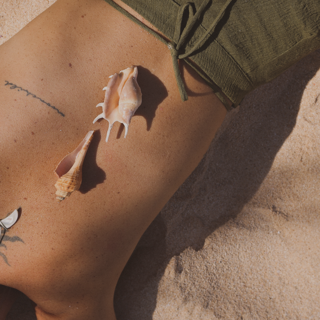 Close-up of a person's tan shoulder and side, with seashells placed on their skin and a green garment.