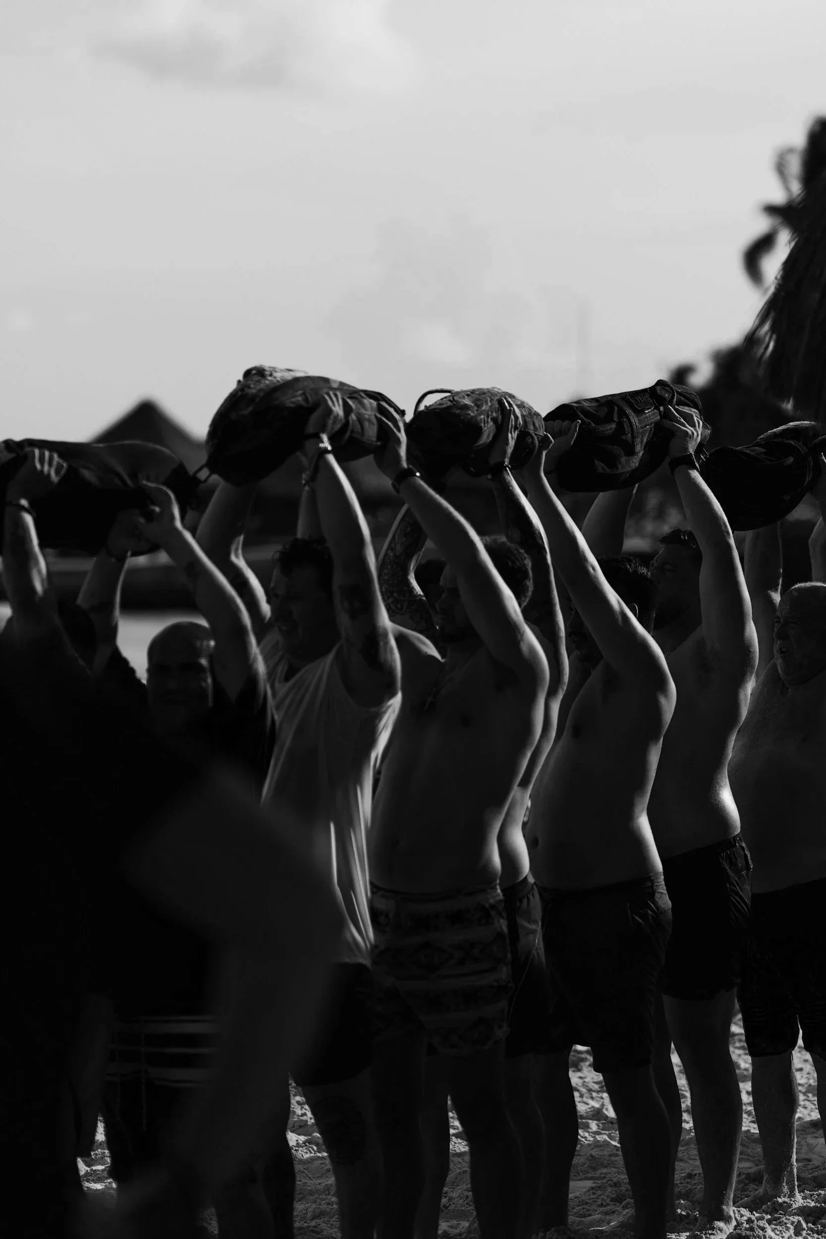 A group of people standing on the beach, holding their hats above their heads, with some wearing swimsuits and shorts, in a line.
