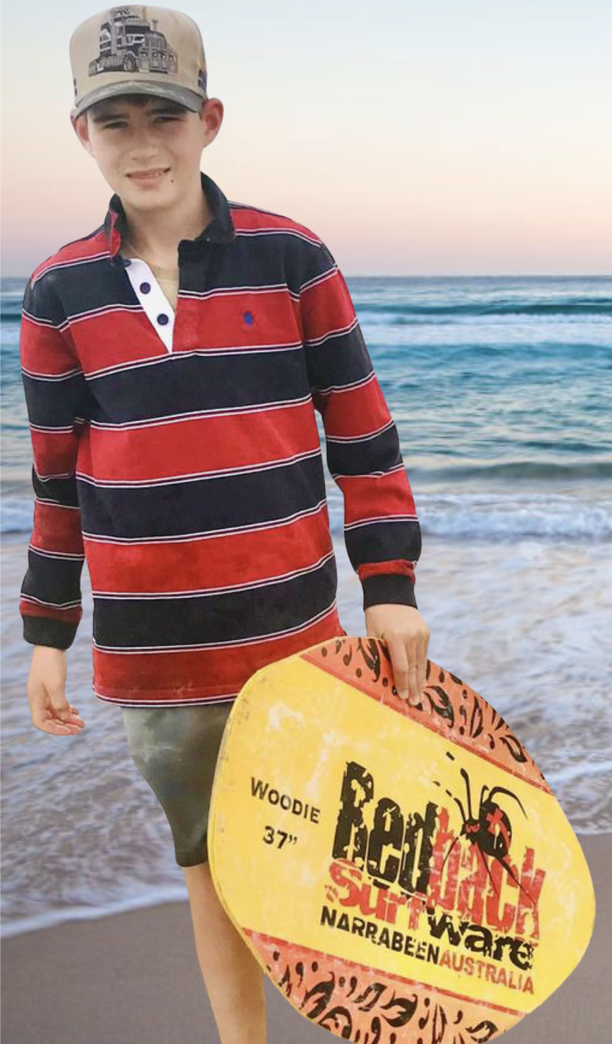 A young man at the beach wearing a beige cap, a red and black striped long-sleeve shirt, and gray shorts, holding a colorful bodyboard with the words 'Beach Surf War' and 'Narrabeen Australia' on it, with ocean waves and a pastel sky in the background.