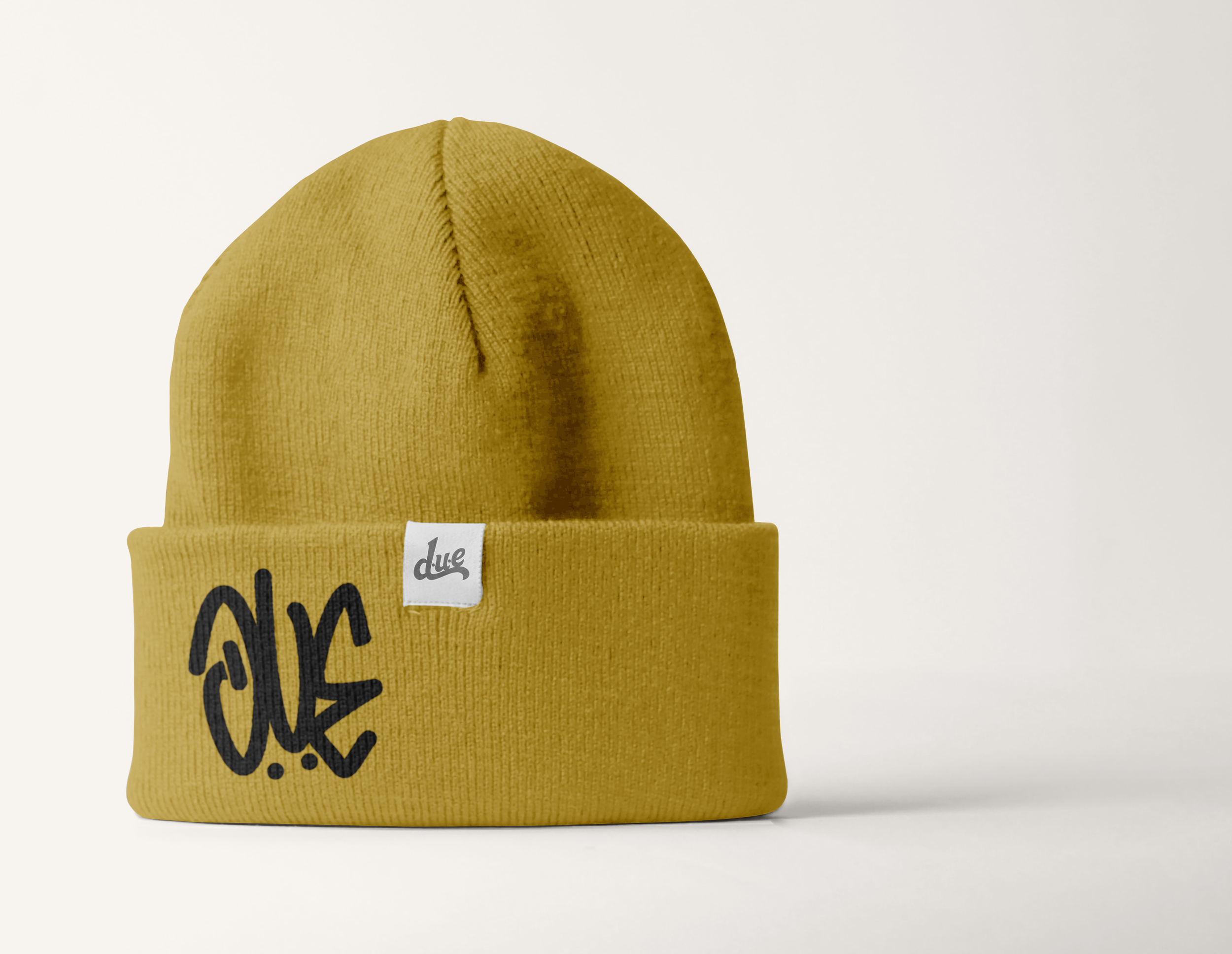 A yellow knit beanie with a white tag that says 'due' and black text on the front, set against a plain white background.