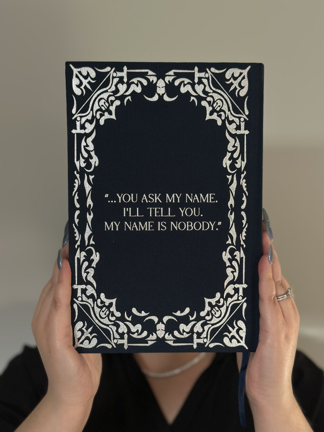 Back cover of The Odyssey collector’s edition held up, featuring silver foil embossing and a Homer quote.