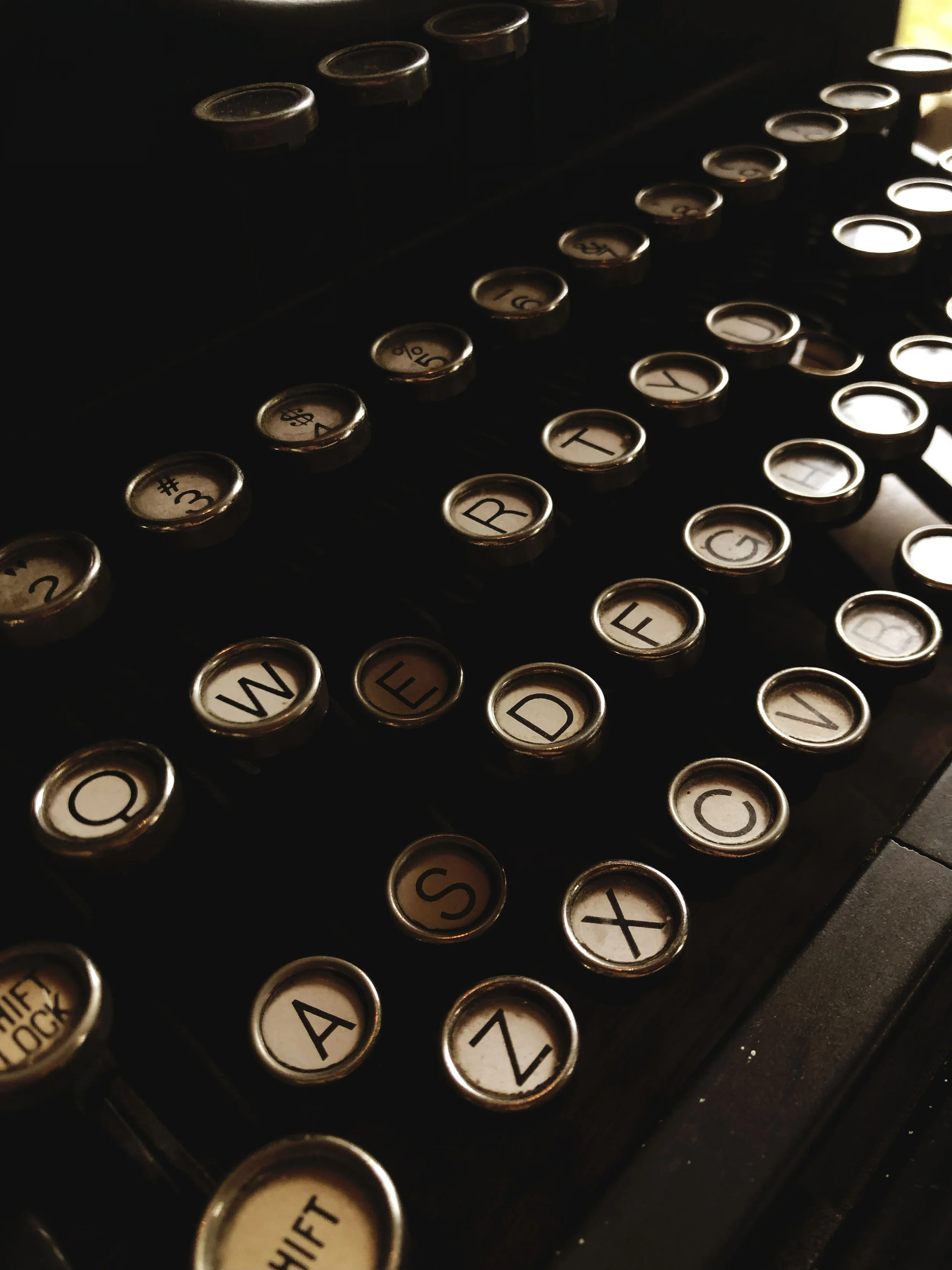 A close-up view of an old-fashioned typewriter's keyboard, showing round keys with black letters on a white background and some black keys in the background.