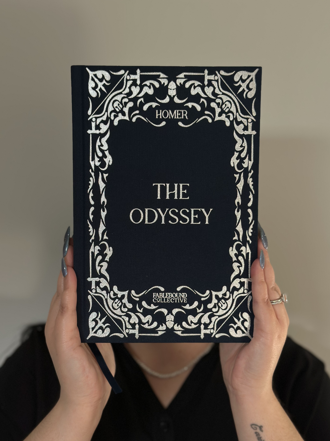 The Odyssey collector’s edition held up to show the navy linen cover and silver foil embossed design.