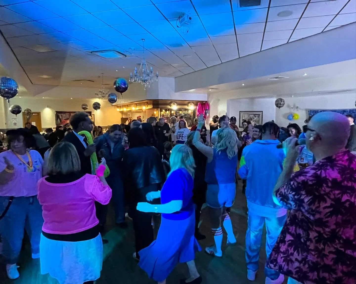 People dancing and socializing at a lively party in a decorated indoor venue with disco balls and dim lighting.