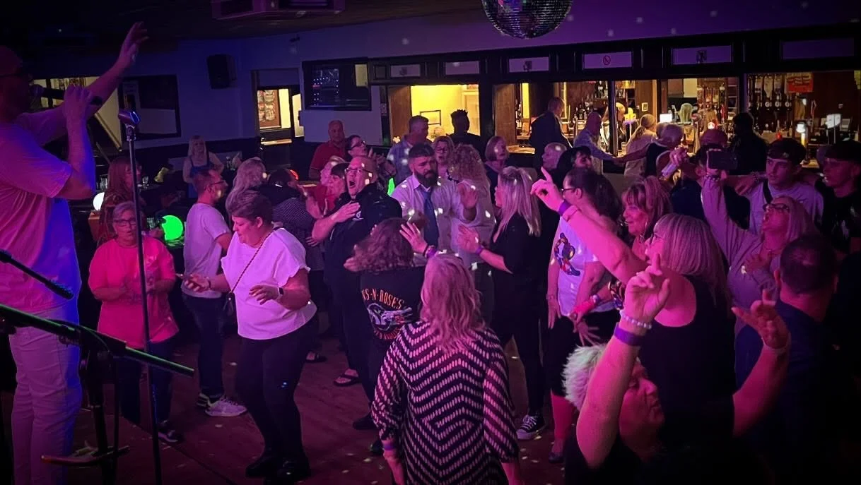 People dancing and socializing at a nightclub with colorful lighting and a bar in the background.