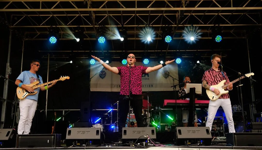 Band performing on an outdoor stage with colorful lighting.