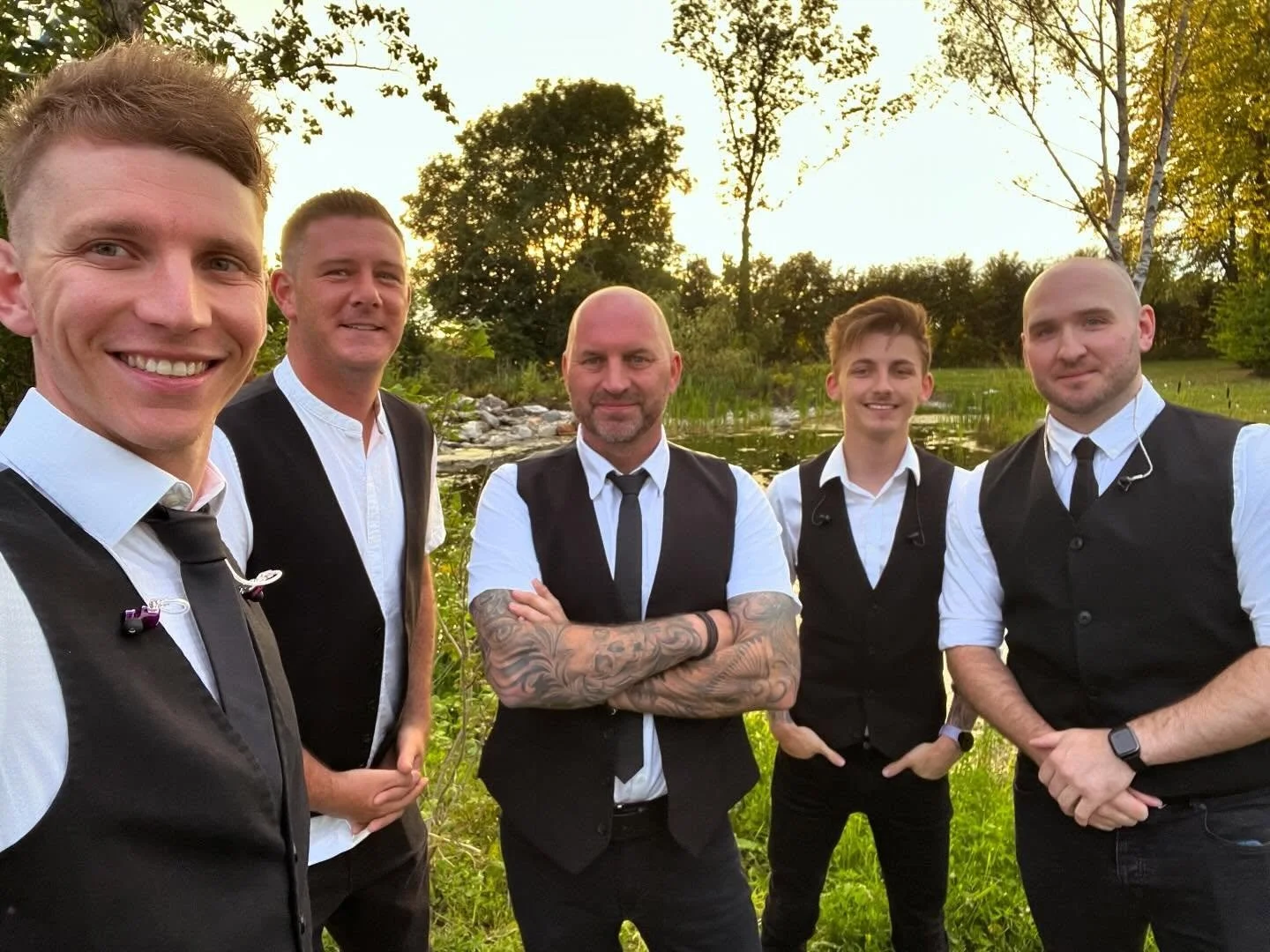 A group of five men taking a selfie on stage during a concert with an excited crowd in the background.