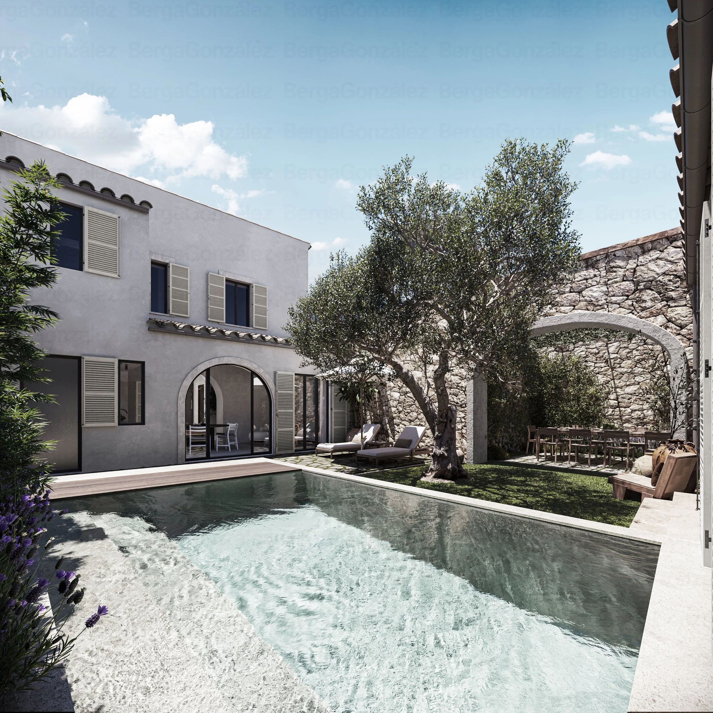 A modern outdoor courtyard with a swimming pool, lounge chairs, a large tree, and a stone wall with an archway, next to a white building with shuttered windows and arched glass doors under a blue sky with clouds.