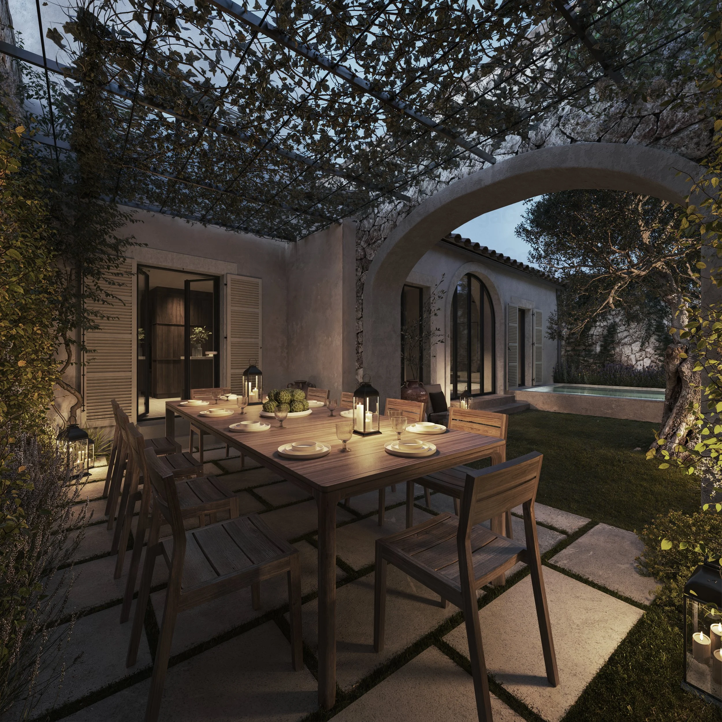 An outdoor dining area at dusk with a wooden table set with plates, glasses, and lanterns, surrounded by chairs. The space is lit with lanterns, features an arched doorway, a window with shutters, and a small pool, all enclosed with trellises and lush greenery.