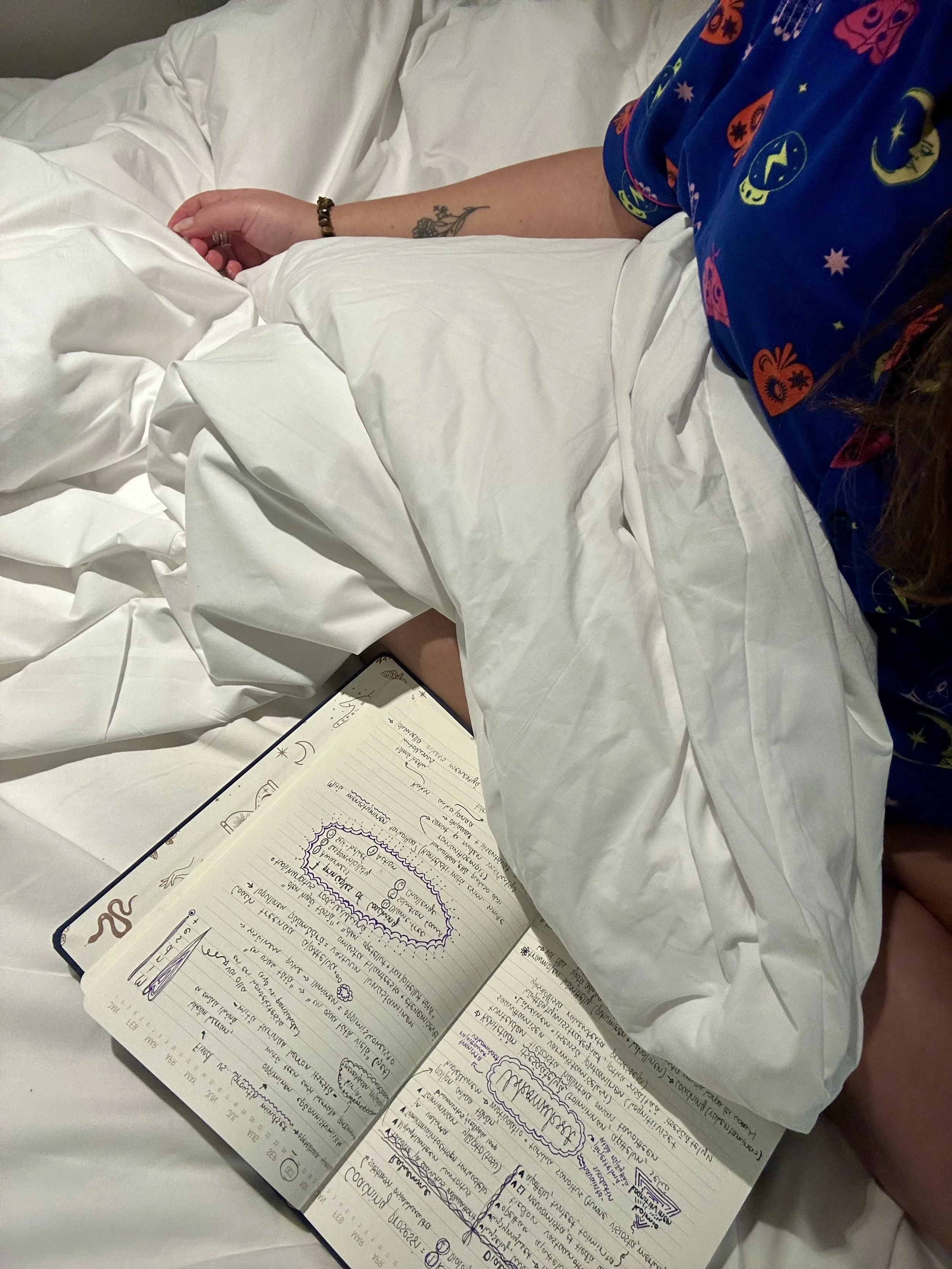 Woman in colourful pyjamas writing in a notebook, reflecting and resting.