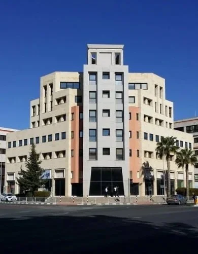 Modern multi-story hotel with a unique geometric facade, palm trees, and a clear blue sky.