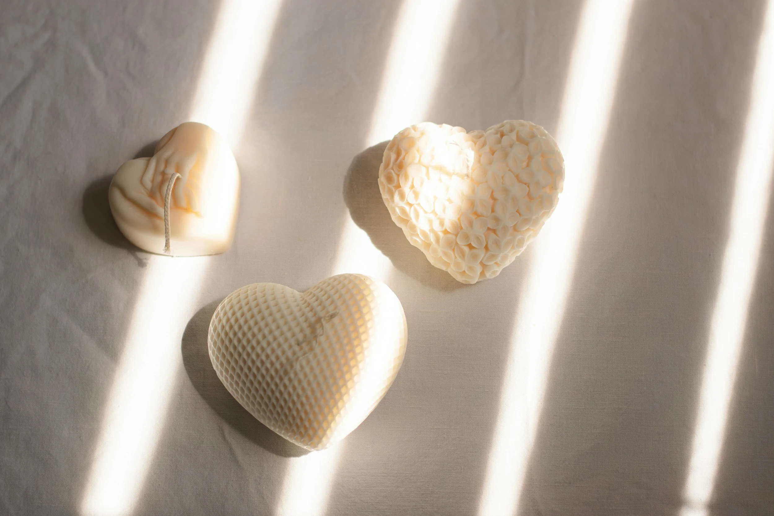 Cuore e altri oggetti decorativi bianchi, con luce naturale che crea linee di ombra sulla superficie