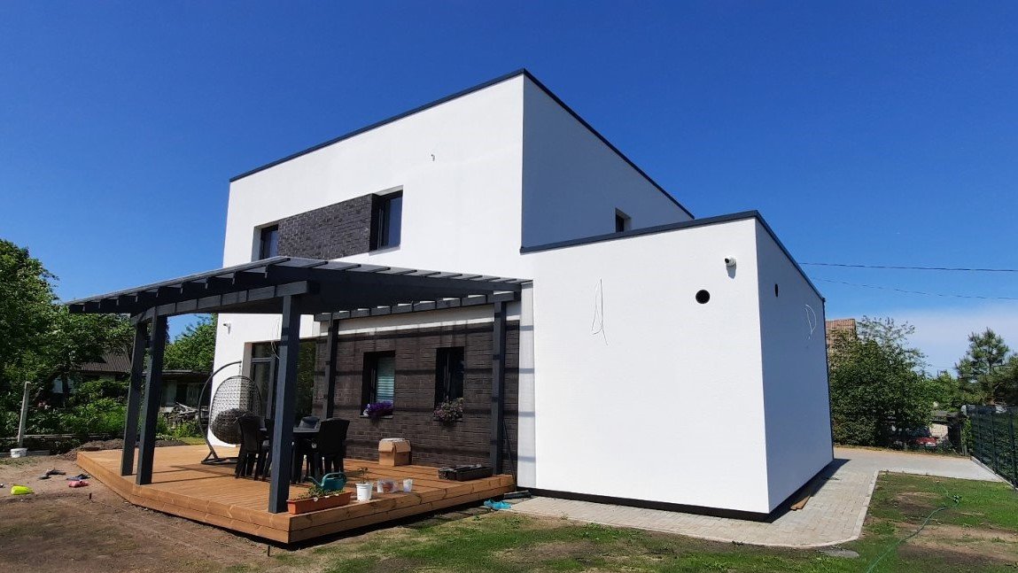 Modern white two-story house with black accents and a wooden patio with outdoor furniture.