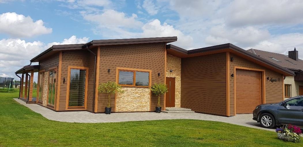 Modern house with wooden and stone exterior, large glass doors, small trees in pots, and a car parked in front.