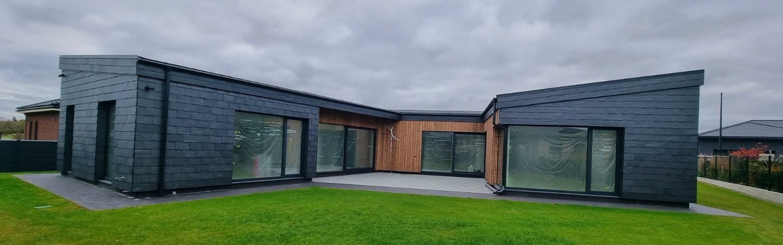 Modern house with black and wooden siding, large glass sliding doors, and a green lawn.