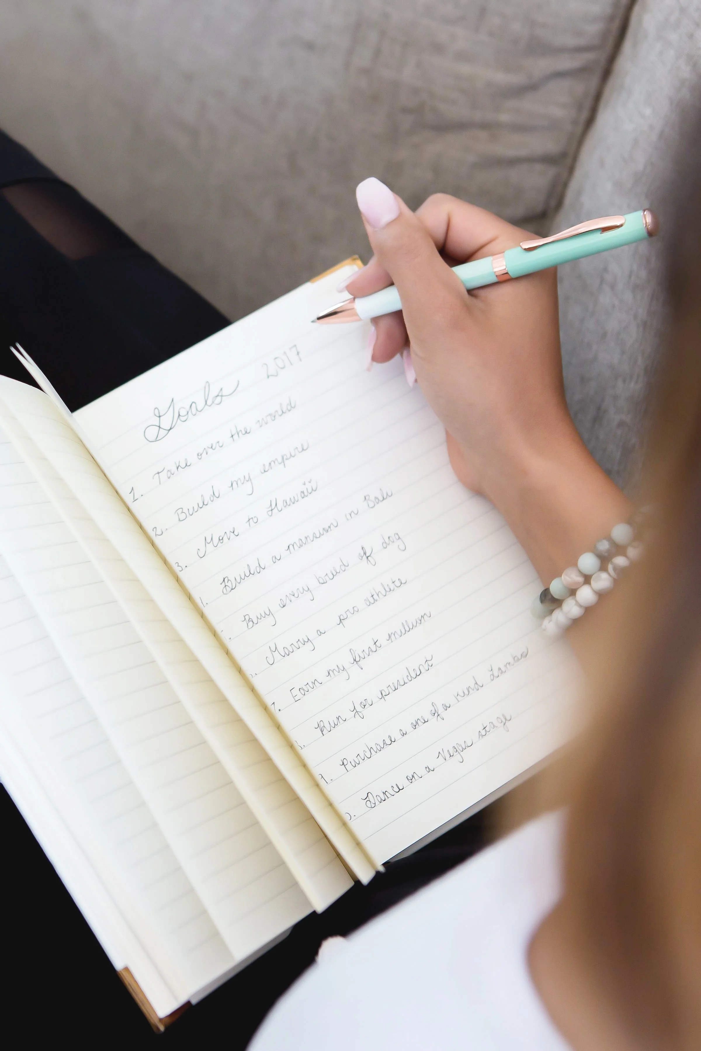 A person writing in a notebook with goals for 2017, including travel and personal achievements, using a pen, with bracelets on their wrist.