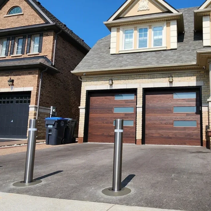 Three stainless steel anti-theft bollards installed across an interlocking stone driveway of a modern, multi-garage Toronto home.
