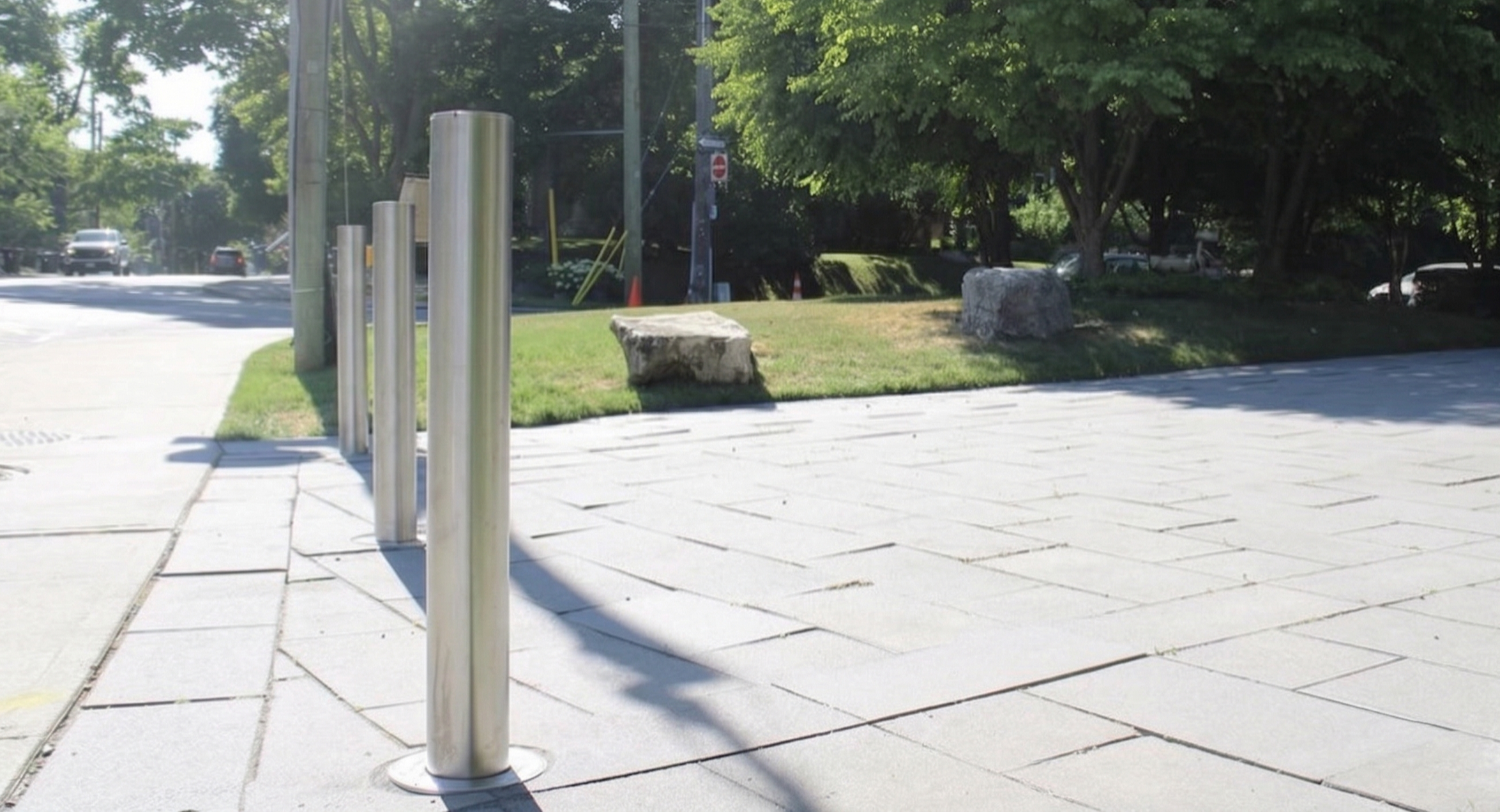 A line of multiple stainless steel retractable bollards protecting the entire entrance of a long, light-colored stone paver driveway in a residential Toronto neighborhood