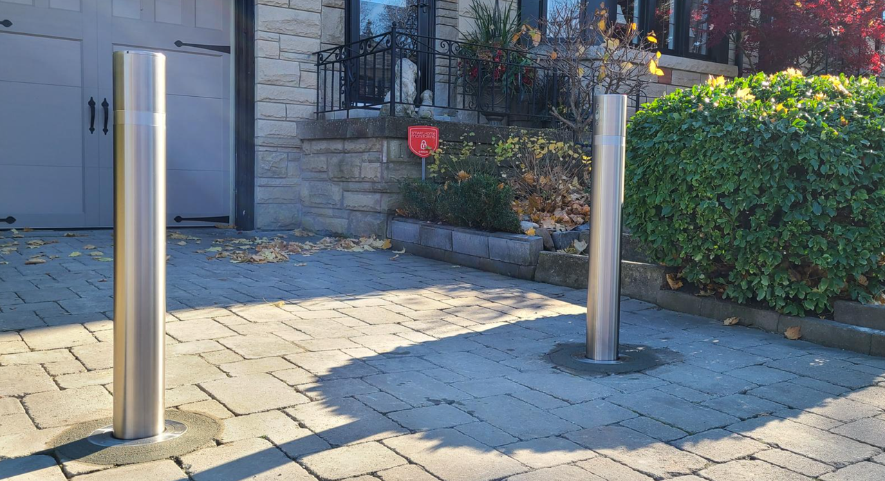 A close-up view of a sleek, single stainless steel retractable security bollard installed in an interlocking stone driveway during autumn in Toronto.