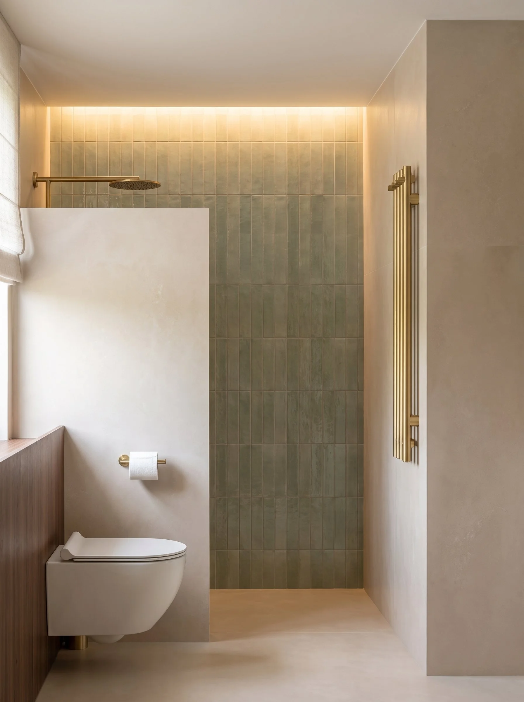 Baño moderno con pared de azulejos verdes, ducha con cabezal fija, radiador dorado y sanitario blanco, con cortina delgada en la esquina izquierda y una papelera debajo del lavabo.