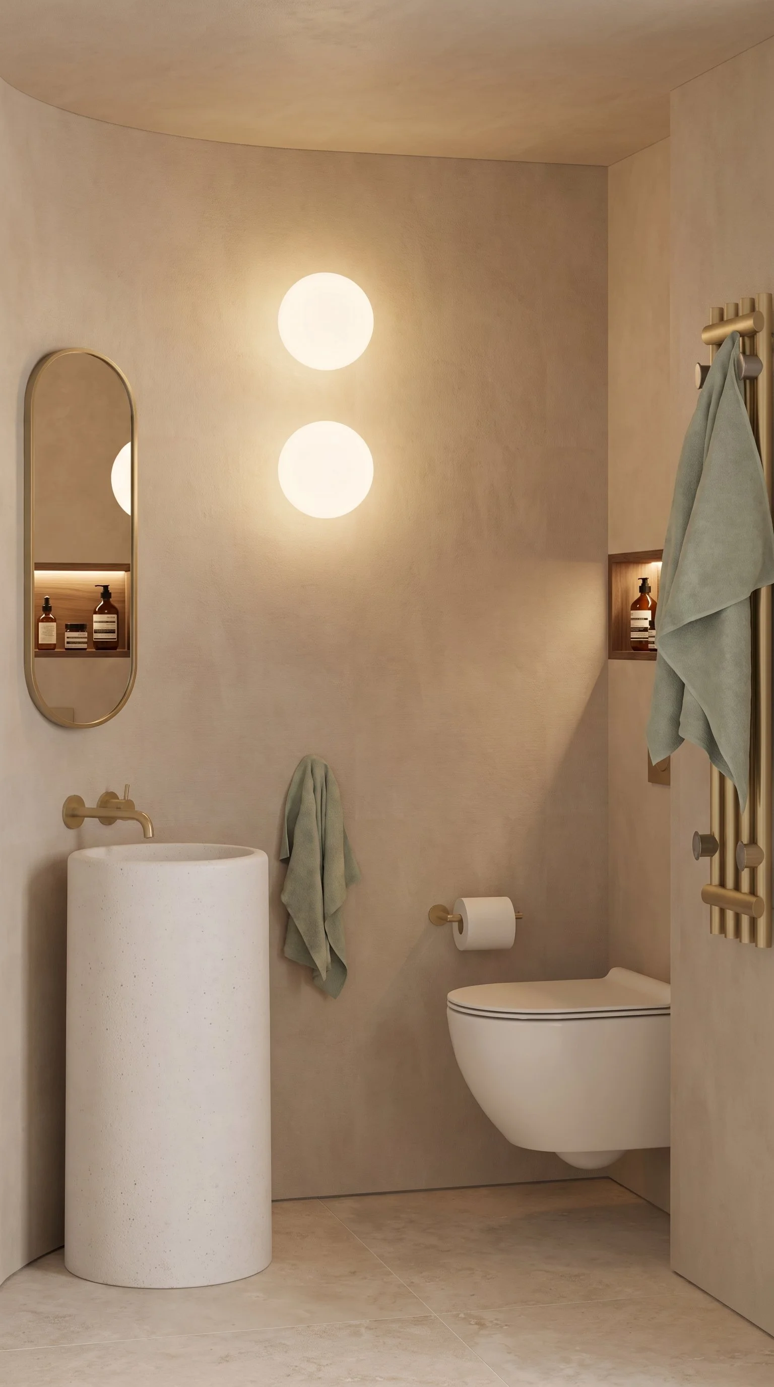 Baño con paredes beige, lavabo de pie, espejo ovalado, luces redondas en la pared, toallas verdes, portalámparas con botella de jabón, inodoro, papel higiénico y radiador de toallas.