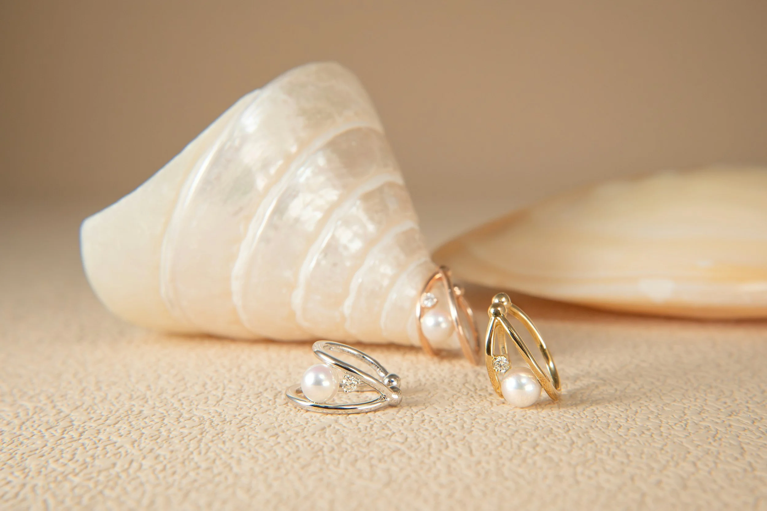 Jewelry set with pearl earrings and ring, displayed with seashells on a textured surface.