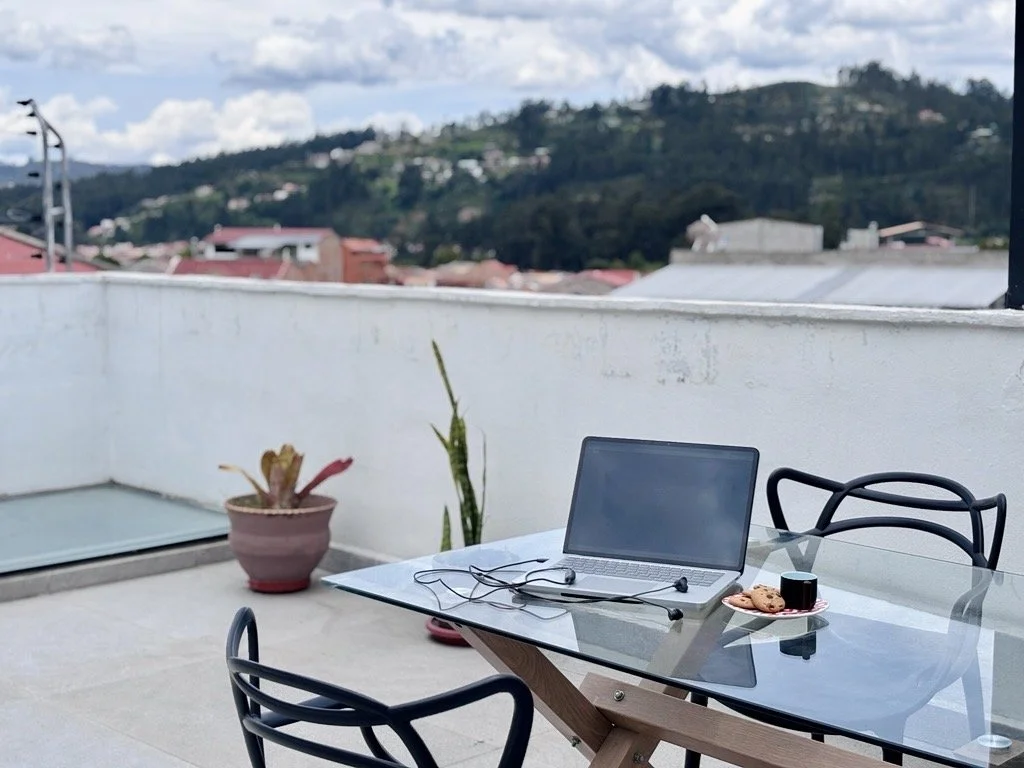 Blick von der Dachterrasse in Cuenca; im Vordergrung ein aufgeklappter Laptop mit Headset und daneben Kekse und eine Espressotasse; alles auf einem Glastisch