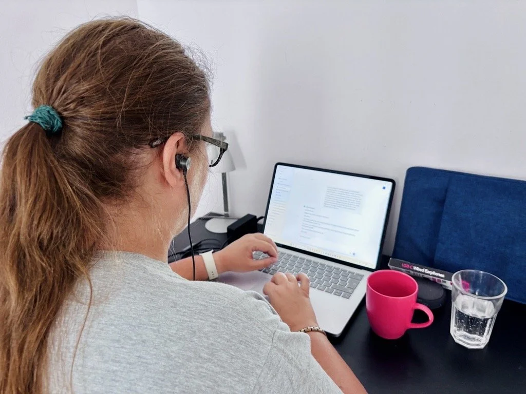 Tamara von seitlich-hinten, aufgeklappter Laptop, Tasse und Wasserglas daneben