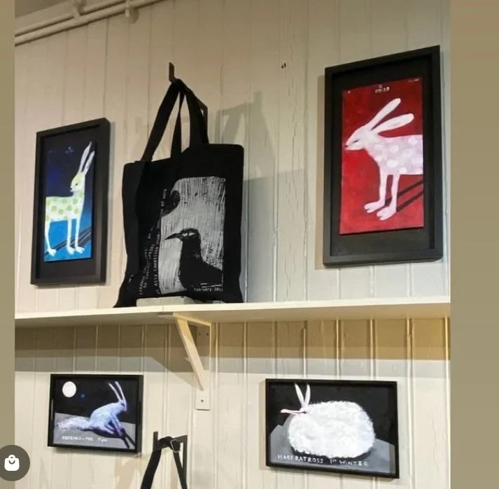 Four framed illustrations of rabbits in different poses and colors on a wall with a black tote bag hanging in the center.