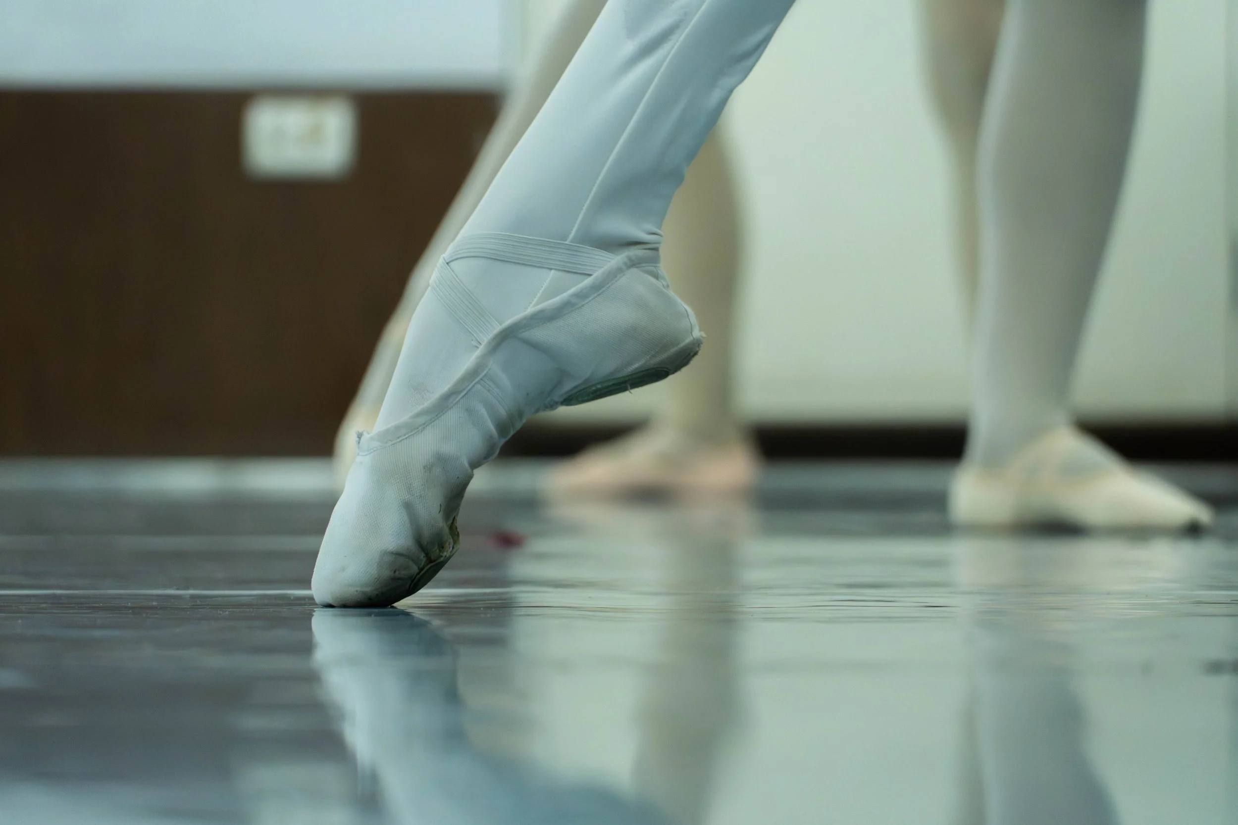 Zapatos de ballet en el suelo, con una bailarina en puntas de pie.