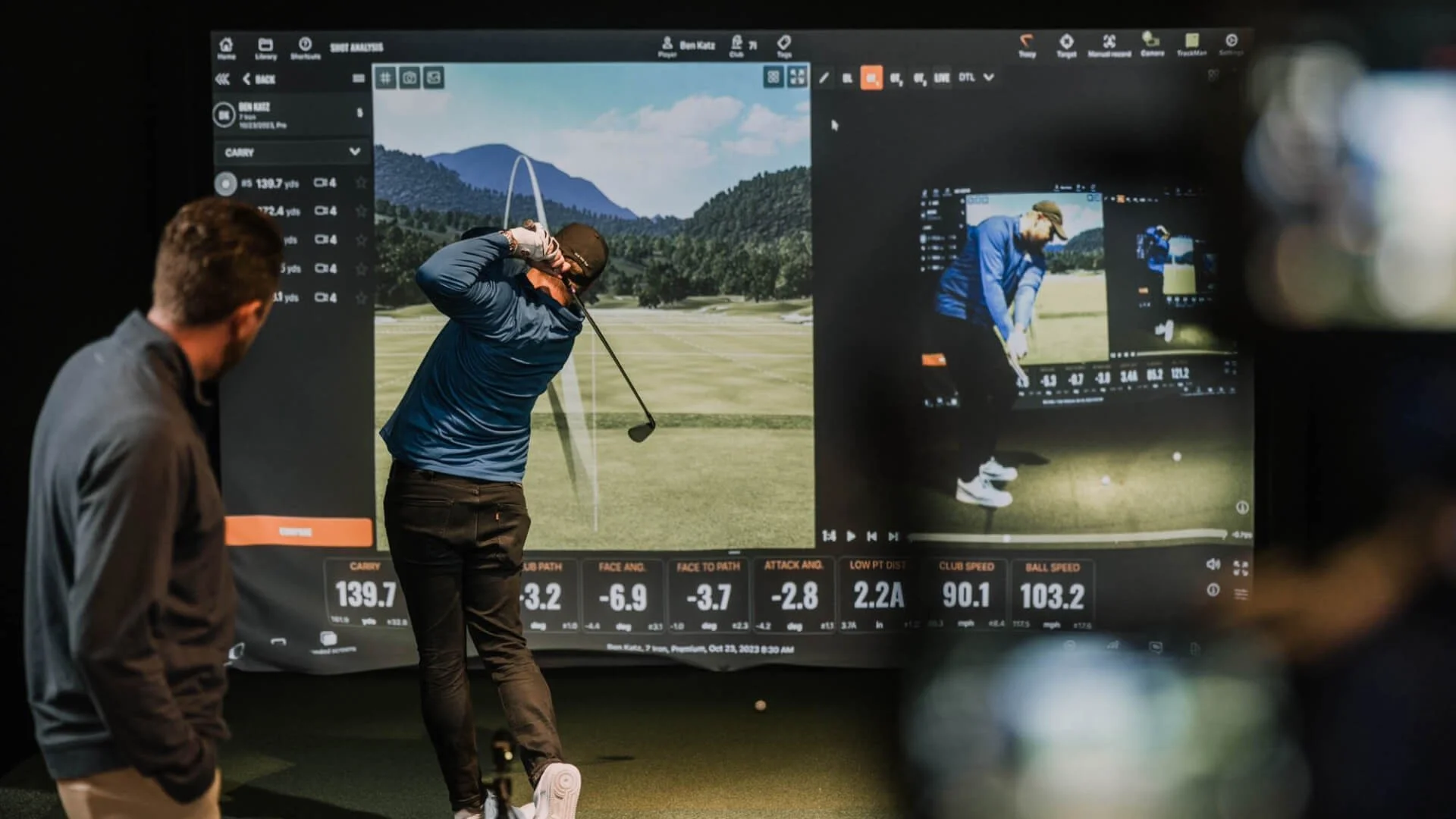 Two men playing golf on the Trackman golf simulator showing their stats.